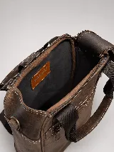 Matera mochila unisex de cuero marrón, con diseño estructurado, bolsillo frontal con cierre, asas superiores y correas ajustables.