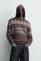 Jersey de punto con textura, corte relajado, cuello redondo y manga larga. Presenta un diseño jacquard geométrico con motivos de copos de nieve en tonos marrones, azules y blancos.