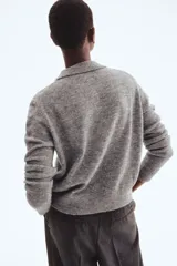 Cárdigan corto de punto suave, color gris jaspeado, con cuello camisero, abotonadura frontal y remates acanalados en puños y bajo.