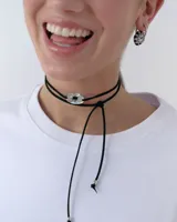 Choker de estilo bolo tie compuesto por un cordón negro largo y un dije central ovalado con diseño de estrella calada en acabado dorado espejado.