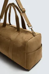 Bolso de viaje de estilo minimalista con acabado liso. Cuenta con un compartimento principal con cierre de cremallera, un bolsillo interior con cierre, un bolsillo frontal plano, asas de mano y un asa de hombro ajustable y extraíble.