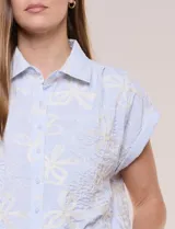 Camisa celeste con bordado floral en color crudo, de corte semi holgado, cuello camisero, manga corta japonesa con dobladillo y cierre frontal de botones.