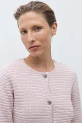 Chaqueta de punto color celeste, con cuello redondo, manga larga y cierre frontal con botones metálicos plateados.