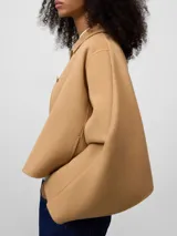 Chaqueta corta color camel con cuello solapa, manga larga japonesa y cierre frontal con botones. Presenta un diseño con capa superpuesta en la espalda.