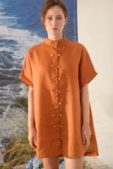 Vestido corto de lino color naranja, con moldería amplia, manga corta, cuello mao y botonadura frontal con botones dorados.