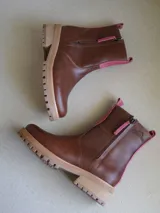 Botas cortas de cuero blanco con suela track marrón y detalles en gamuza beige en la parte frontal y trasera. Cuenta con cierre lateral y tirador de cuero.