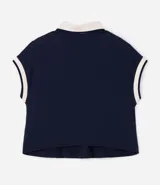Chomba azul marino de corte boxy y manga corta, confeccionada en tejido piquet de algodón. Cuenta con cuello polo y ribetes en las mangas de color beige contrastante, además de una botonera frontal corta.