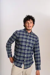 Camisa de manga larga confeccionada en tejido de franela con estampado de cuadros en tonos azul marino y verde. Presenta cuello abotonado, cierre frontal con botones y un bolsillo en el pecho con el logo bordado de la marca.