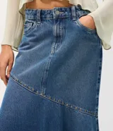 Pollera midi de jean azul, de tiro medio con pretina y pasacintos. Presenta un recorte diagonal en la parte inferior decorado con pequeñas tachas metálicas.