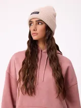 Gorro tipo beanie de punto acanalado en color beige, con parche rectangular negro con el logo de la marca en el frente.