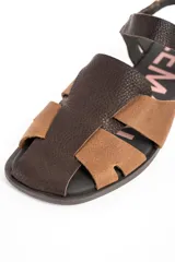 Sandalias cangrejeras de cuero tipo flats, con diseño bicolor en tonos marrón y tostado, tiras entrelazadas en el empeine y tira ajustable con hebilla en el talón.