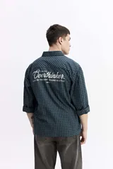 Camisa de popelina a cuadros en tonos azul marino y verde, con bolsillo frontal y estampado en la espalda que dice "COOL BUT OVERTHINKER. LOST IN THOUGHT. FOUND IN STYLE".