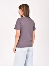 Remera lila de corte recto y mangas cortas, con estampado pequeño de un gato blanco con gorro rojo, gafas de sol y copa de vino, junto a la frase 'J'adore'.