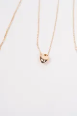 Set de cuatro collares de cadena fina en color dorado. Incluye una cadena simple, una con dije de corazón, una con detalles de perlas pequeñas y una con dijes colgantes en forma de cruz.