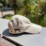 Gorra de cuero metalizado dorado, con ojales metálicos decorativos y etiqueta de marca aplicada en el lateral.