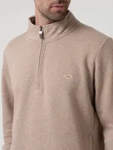Buzo de hombre con medio cierre frontal y cuello alto, confeccionado en algodón orgánico con interior de french terry. Presenta un diseño liso en color taupe con un pequeño logo bordado en el pecho.