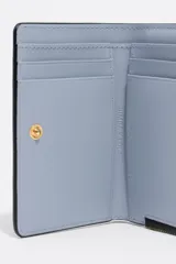 Billetera compacta de cuero vacuno en color negro, con cierre superior metálico dorado y logo de la marca estampado en el frente.