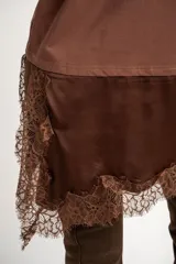 Remera oversize marrón con corte a la altura de la cadera, cuello redondo y mangas cortas holgadas. Incorpora un aplique inferior superpuesto de satén con detalles de encaje bordado en los bordes.