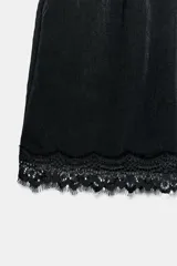 Shorts de satén negro con cintura elástica en la espalda, bolsillos delanteros y detalles de puntilla a tono en el ruedo.