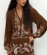Vestido midi de viscosa color marrón con estampado paisley en tonos claros. Presenta cuello alto, mangas largas con puños ajustados y un lazo frontal en la cintura que permite entallar la prenda.