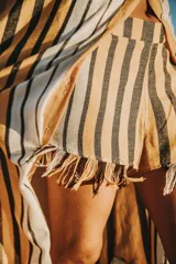 Short tejido en telar de algodón a rayas horizontales en tonos beige, blanco y negro, con elástico en la cintura y flecos en el ruedo.