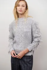 Buzo de punto color gris claro melange, con cuello redondo, mangas largas con flecos y trenzas en el frente.