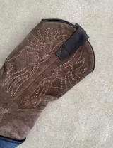 Botas de cuero color marrón y blanco con bordados negros, de estilo cowboy con taco bajo.