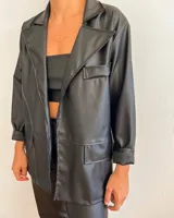 Blazer negro de cuerina con solapas, bolsillos frontales y corte holgado.