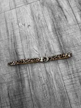 Cinto de cuero sintético con estampado animal print y hebilla metálica plateada.