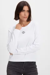 Remera de manga larga con textura acanalada y silueta ajustada. Presenta cuello redondo y un pequeño bordado decorativo en el centro del pecho.