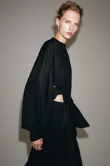 Camisa negra de cuello redondo y manga larga ancha con silueta fluida, con cierre frontal de botones y aberturas laterales en el bajo.