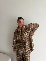 Camisa de viyela con estampado de cuadros en tonos marrones, beige y negro. Presenta cuello clásico, cierre frontal con botones, mangas largas con puños abotonados y dos bolsillos delanteros con solapa.