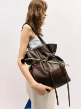 Bolso tipo tote de cuero vacuno marrón, de gran tamaño y diseño liviano. Cuenta con doble asa de hombro y detalle de correa ajustable con nudo en el frente.