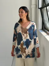 Sweater de tejido de punto con estampado abstracto en tonos azul, marrón y beige. Presenta cuello en V, mangas largas con puños vueltos y un corte holgado.