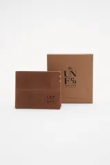 Billetera de cuero marrón con pespuntes decorativos y logo grabado en el frente. Interior con compartimentos y forro de algodón.