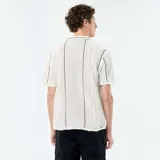 Camisa de manga corta confeccionada en tejido de punto fantasía color beige, con cuello camisero, cierre frontal de botones y detalles de líneas oscuras en zigzag.