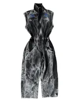 Mono de jean con lavado gris efecto desgastado, con múltiples cortes estructurales, cierre frontal oculto por cartera, cintura elástica y bordado de logo en azul. Incluye un pequeño accesorio de bolso desmontable para la cintura.