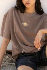 Remera oversize de algodón con efecto lavado, color negro, de manga corta y cuello redondo. Presenta una estampa gráfica en la espalda con motivos solares y tipografía en tonos naranja y amarillo.