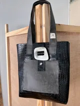 Bolso tote negro con textura símil cuero de cocodrilo, bolsillo frontal de cuero liso y cierre con botón metálico.
