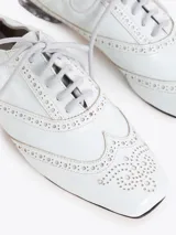 Zapato de cuero vacuno color blanco con acabado arrugado, diseño estilo oxford con detalles perforados, cordones y tacón bajo decorado con pedrería.