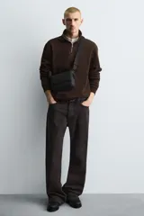 Bandolera verde militar con acabado engomado y textura geométrica. Tiene un compartimento principal con cierre de solapa y botón a presión, un bolsillo interior con cremallera y un asa de hombro ajustable con monedero.