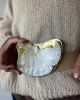 Cinturón de cuero color tostado con hebilla grande irregular de nácar con borde dorado.