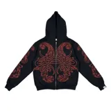 Hoodie con cierre frontal completo, confeccionado en algodón de tejido grueso. Presenta un diseño estampado en serigrafía con motivos de hojas de acanto en color rojo sobre fondo negro. Cuenta con bolsillos laterales y cierre metálico YKK.