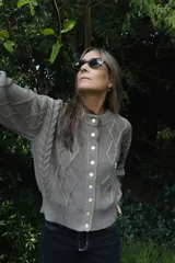 Saco tejido de punto con diseño de ochos y trenzas, color azul marino. Presenta cierre frontal con botones en contraste de color turquesa y un delicado bordado a mano en el pecho.