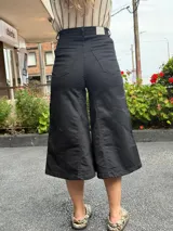 Jean capri negro de tiro alto con diseño de pierna amplia tipo culotte, confeccionado en denim con lycra, bolsillos y botón frontal.