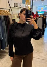 Blusa de satén color negro con cuello alto, mangas largas con detalle de botones laterales y lazo decorativo en el hombro.