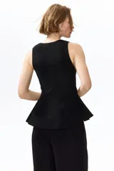 Chaleco negro de punto acanalado, sin mangas, con cuello redondo y cierre frontal de botones. Presenta un diseño entallado con bajo en peplum.