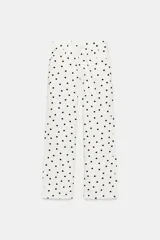 Jeans de tiro bajo con diseño de pierna ancha y corte largo. Presenta un estampado de lunares negros sobre fondo blanco, cierre frontal con cremallera y botón metálico, y cinco bolsillos.