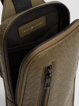 Cartera tipo sling Tommy Hilfiger de color verde militar, con diseño de monograma TH en relieve, bolsillo exterior con cierre y correa ajustable negra.