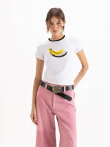 Remera blanca de manga corta, con ribetes negros en el cuello y estampa frontal de una banana estilo pop art.